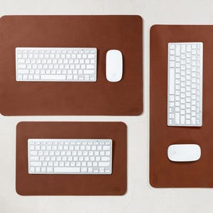 May include: A collection of brown rectangular desk pads with rounded corners, each featuring a white keyboard and mouse. The pads vary in size, with the largest measuring approximately 30 inches long. The keyboards have a standard layout.