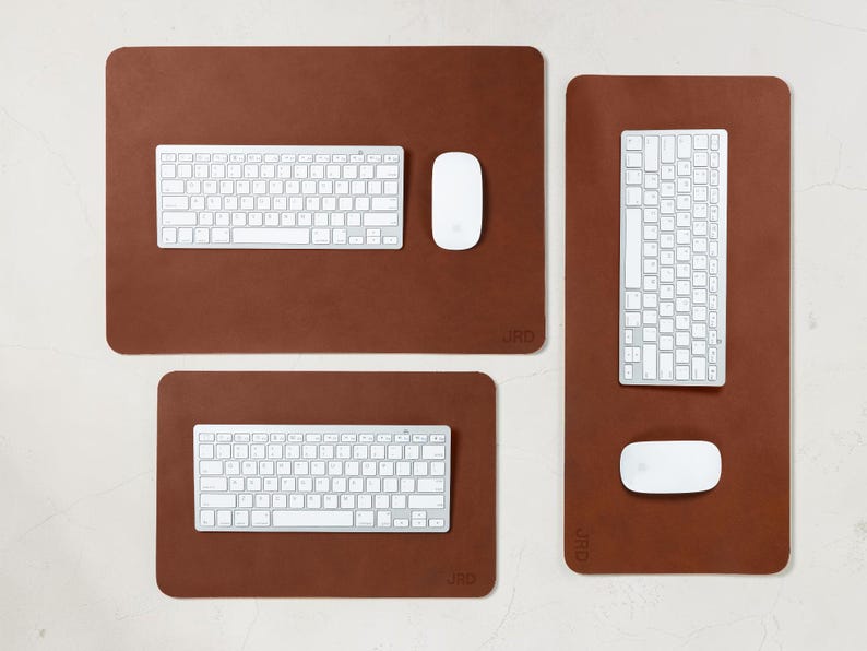May include: A collection of brown rectangular desk pads with rounded corners, each featuring a white keyboard and mouse. The pads vary in size, with the largest measuring approximately 30 inches long. The keyboards have a standard layout.