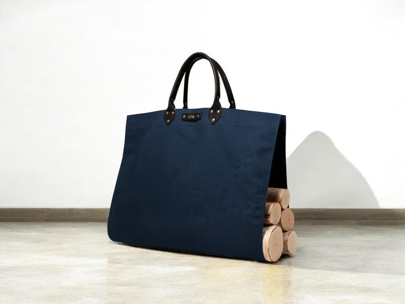 May include: A navy blue canvas tote bag with black leather handles and brass rivets. The bag is filled with firewood. The bag has a small leather tag with gold lettering.