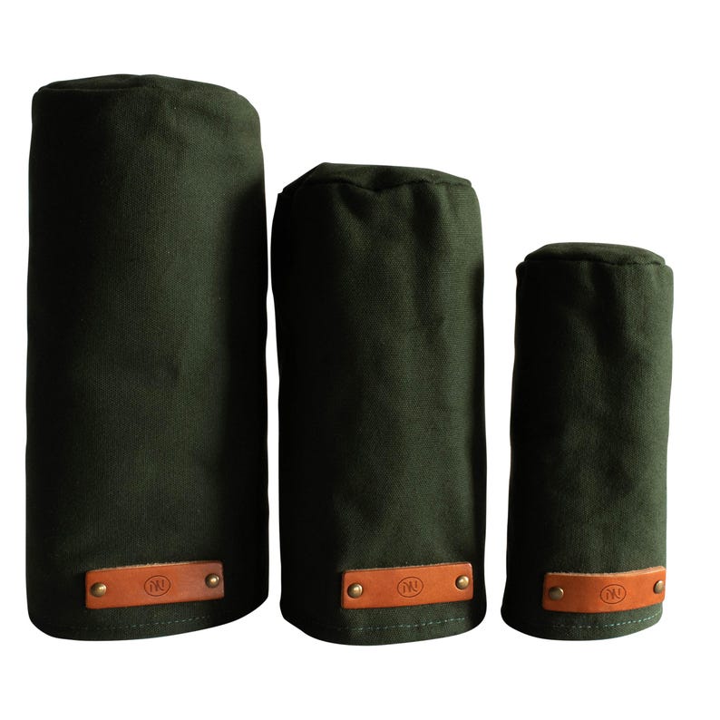 May include: Three cylindrical olive green fabric covers of varying heights, each featuring a rectangular tan leather patch at the base secured with two brass-toned metal rivets. Each leather patch is embossed with a circular logo containing the letters NN.