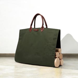 May include: An olive green canvas tote bag with brown leather handles and accents. The bag is filled with several cut logs. The bag has a rectangular shape and is designed for carrying firewood.