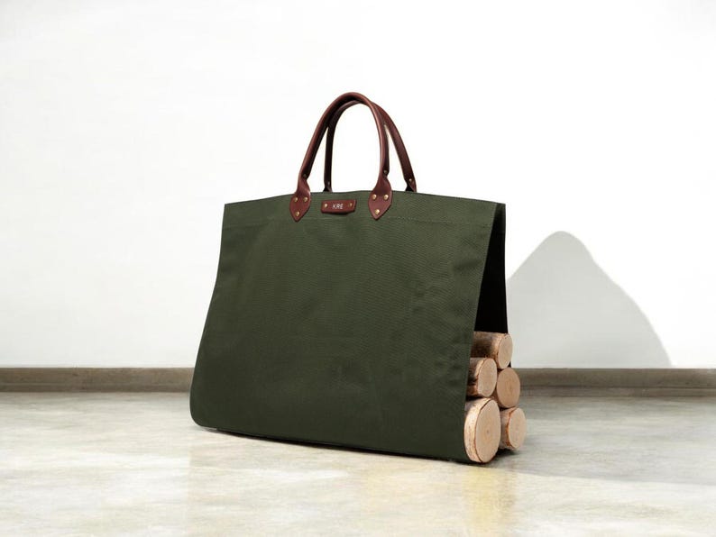 May include: An olive green canvas tote bag with brown leather handles and accents. The bag is filled with several cut logs. The bag has a rectangular shape and is designed for carrying firewood.