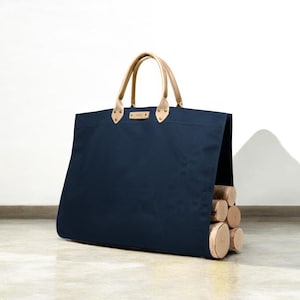 May include: A navy blue tote bag with light brown leather handles and accents. The bag is filled with several pieces of firewood. The bag has a rectangular shape and is designed for carrying firewood.