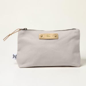 May include: A light gray canvas pouch with a brass nameplate that reads "RL". The pouch has a zipper closure and a leather pull. A small tag with a black and white design is attached to the side.
