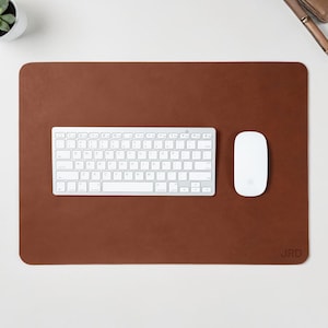 May include: A brown leather desk mat with a white keyboard and mouse. A small succulent plant in a white pot is in the upper left corner. The initials "JRD" are embossed in the lower right corner.