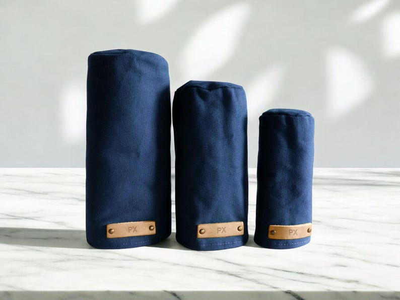 May include: Three navy blue golf club head covers of varying heights, each featuring a rectangular tan leather patch at the base. The leather patches are secured with two metal rivets and are embossed with the letters PX in a simple font.