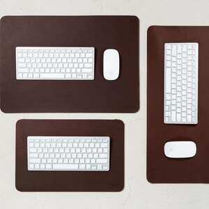 May include: A top-down view of three brown rectangular desk pads with rounded corners. Each pad has a white keyboard and a white mouse. The pads vary in size, with the largest at the top and the smallest at the bottom.