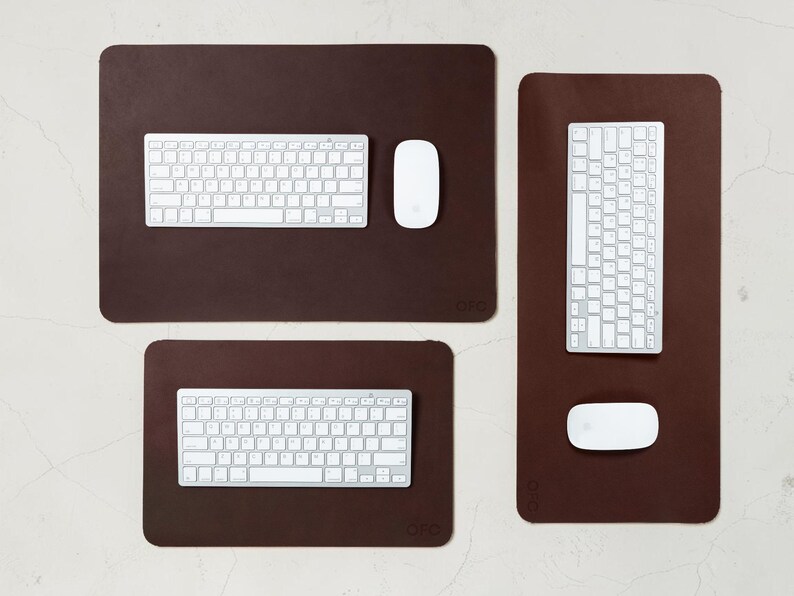 May include: A top-down view of three brown rectangular desk pads with rounded corners. Each pad has a white keyboard and a white mouse. The pads vary in size, with the largest at the top and the smallest at the bottom.