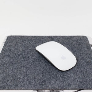 Puede incluir: Una alfombrilla de ratón de fieltro gris con un ratón inalámbrico blanco en la parte superior.