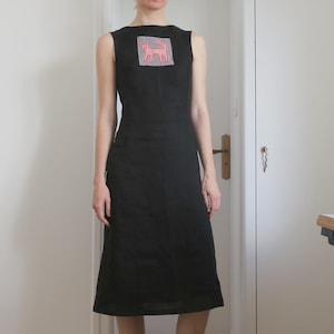 May include: A black sleeveless dress with a square neckline. The dress has a pink and red animal graphic on the chest. The person is wearing white socks and canvas trainers.