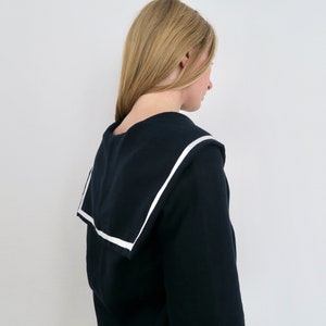 May include: A black sweater with a white sailor collar. The sweater is long-sleeved and has a relaxed fit.