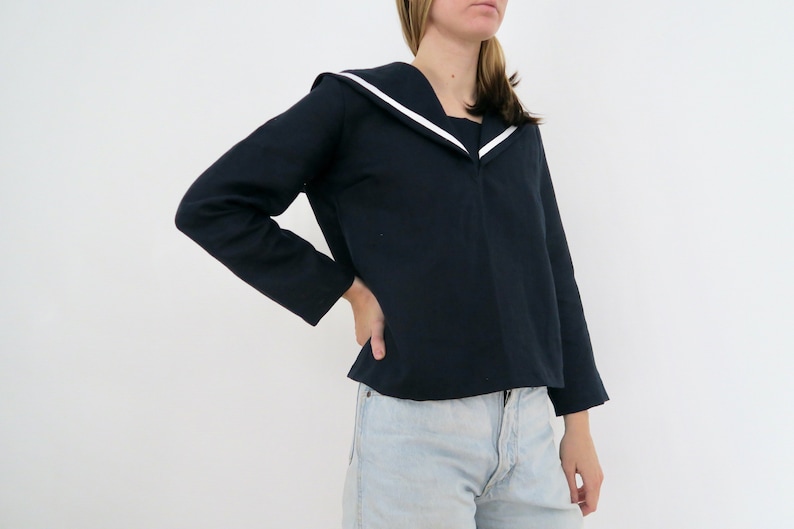May include: A navy blue long-sleeved shirt with a wide white sailor collar. The shirt has a cropped length and is made of a soft, comfortable fabric.