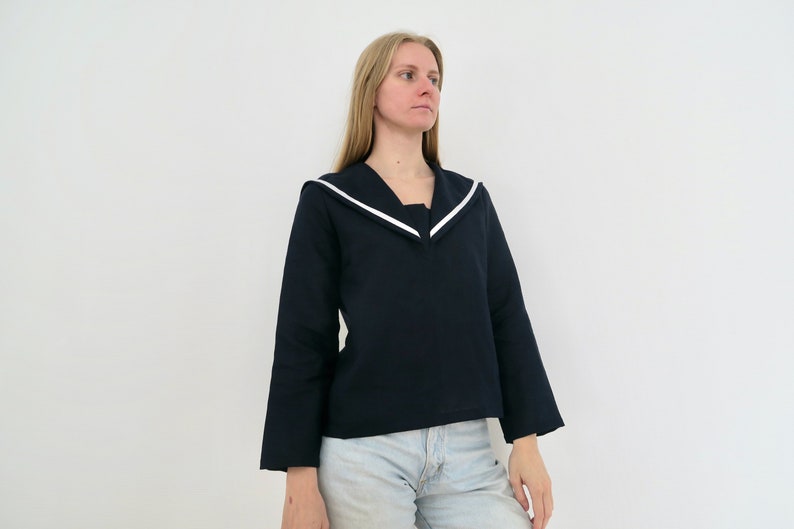 May include: A navy blue long-sleeved shirt with a white sailor collar. The shirt has a relaxed fit and is cropped at the waist.