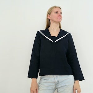 May include: A woman wearing a navy blue long-sleeved shirt with a white sailor collar and light blue jeans.