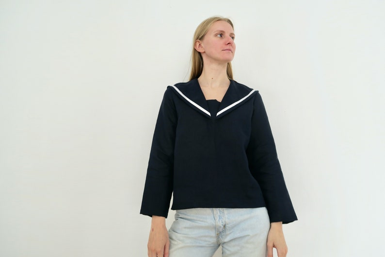 May include: A woman wearing a navy blue long-sleeved shirt with a white sailor collar and light blue jeans.
