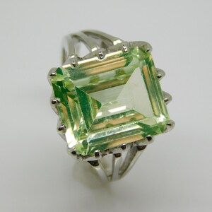 May include: A silver ring with a large, light green emerald-cut gemstone.