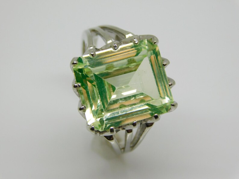 May include: A silver ring with a large, light green emerald-cut gemstone.