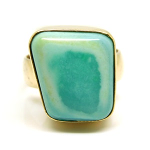May include: A gold ring with a large, rectangular, green gemstone. The gemstone has a white pattern.