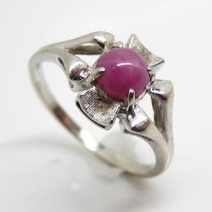 May include: A silver ring featuring a vibrant, round, magenta-colored gemstone at its center. The ring's design includes stylized, openwork floral elements that cradle the gemstone, creating a unique and elegant piece of jewelry.