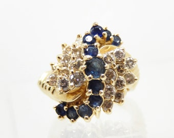 May include: A gold ring with a cluster of blue sapphires and diamonds. The sapphires are set in a swirl pattern and the diamonds are set in a cluster around the sapphires.