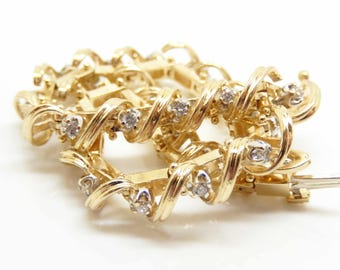 May include: A gold bracelet with a twisted design, featuring small, clear gemstones. The bracelet is made of polished gold and has a secure clasp. The jewelry is displayed on a white surface.