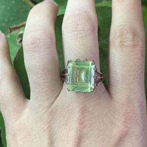 May include: A silver ring with a large, light green, emerald-cut gemstone.