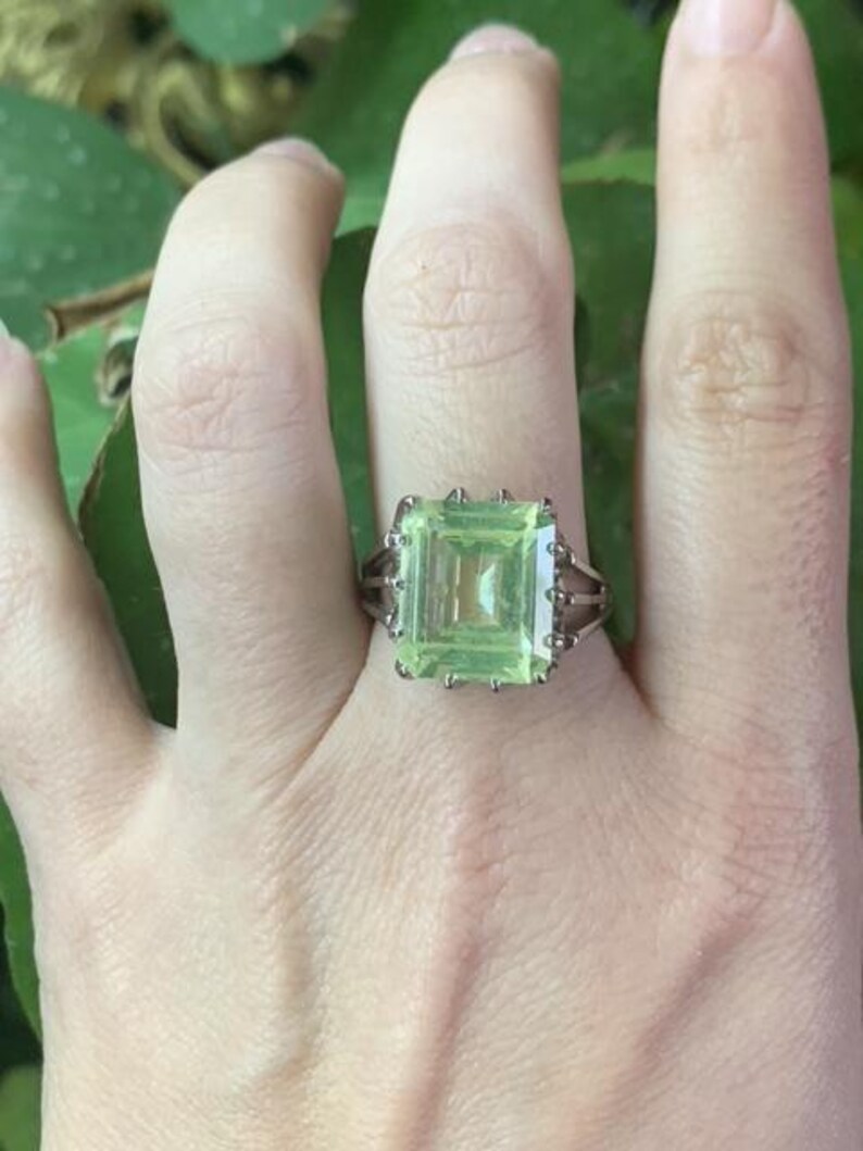 May include: A silver ring with a large, light green, emerald-cut gemstone.