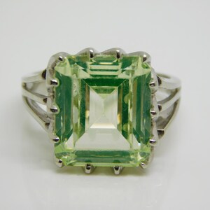 May include: A silver ring with a large, light green, emerald-cut gemstone.