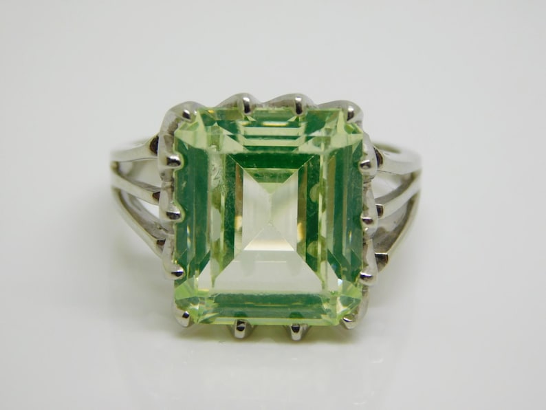 May include: A silver ring with a large, light green, emerald-cut gemstone.