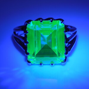 May include: A silver ring with a large, bright green, square-shaped gemstone. The ring is set in a claw setting.