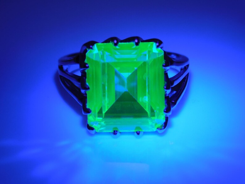 May include: A silver ring with a large, bright green, square-shaped gemstone. The ring is set in a claw setting.