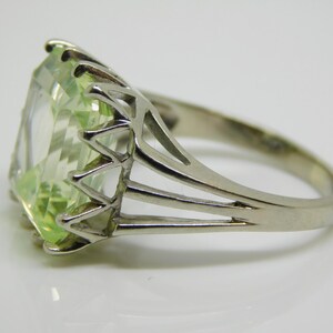 May include: A silver ring with a large, light green, emerald-cut gemstone. The ring has a delicate, openwork band.