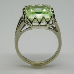 May include: A silver ring with a large, light green, emerald-cut gemstone set in a delicate, open-work setting.