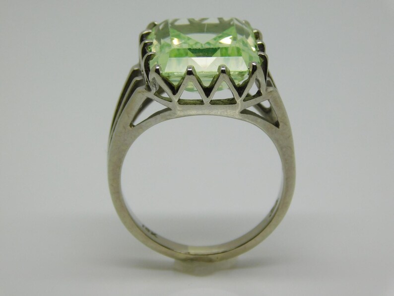 May include: A silver ring with a large, light green, emerald-cut gemstone set in a delicate, open-work setting.