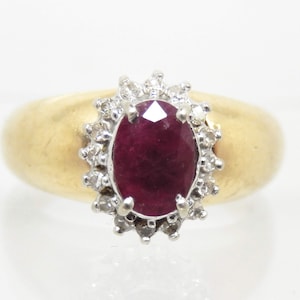 May include: A gold ring with a large oval ruby surrounded by a halo of smaller diamonds.