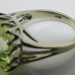 May include: A green gemstone ring set in a silver band with a delicate, intricate design. The band is marked "18K".