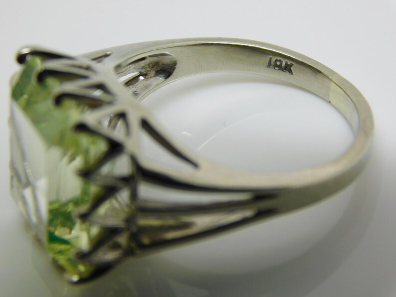 May include: A green gemstone ring set in a silver band with a delicate, intricate design. The band is marked "18K".