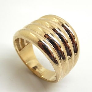 May include: A polished gold ring featuring a wide, domed band with three distinct, parallel horizontal ridges that wrap around the circumference. The metal surface is smooth and reflective, showcasing a continuous, rounded design throughout the piece.