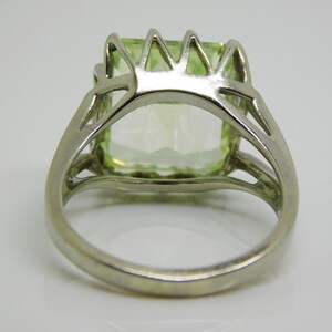 May include: A silver ring with a large, light green gemstone set in a prong setting. The ring has a delicate, openwork design.