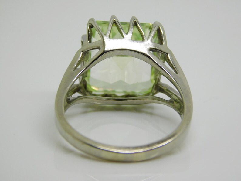 May include: A silver ring with a large, light green gemstone set in a prong setting. The ring has a delicate, openwork design.