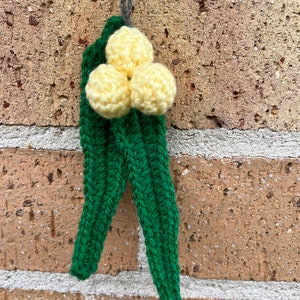 May include: A crocheted yellow flower with green leaves hanging from a brick wall.