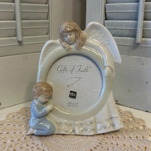 May include: A ceramic photo frame with an angel and a praying child. The frame is off-white with the words "Gifts of Faith". The photo area is 3.5 x 2.5 inches (8.89 x 6.35 cm).