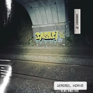 May include: Aerosol Works Volume 1 album cover. The image shows a graffiti-covered brick wall under a concrete archway, with train tracks in the foreground. The graffiti is yellow and black. A white label with the text "AEROSOL WORKS Volume 1" is at the bottom.
