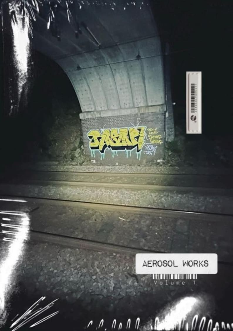 May include: Aerosol Works Volume 1 album cover. The image shows a graffiti-covered brick wall under a concrete archway, with train tracks in the foreground. The graffiti is yellow and black. A white label with the text "AEROSOL WORKS Volume 1" is at the bottom.