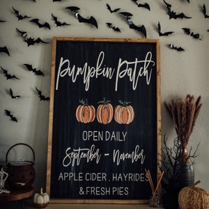 May include: A black chalkboard sign with white lettering that reads "Pumpkin Patch" with three orange pumpkins and the text "Open Daily September - November Apple Cider. Hayrides & Fresh Pies".