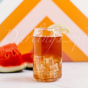 May include: A glass of iced tea with a lemon wedge, served in a can-shaped glass. The drink is surrounded by slices of watermelon.