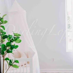 Può includere: Un lettino bianco con un baldacchino bianco drappeggiato sopra. Il lettino ha un materasso bianco e un cuscino bianco. Una pianta verde è in primo piano.