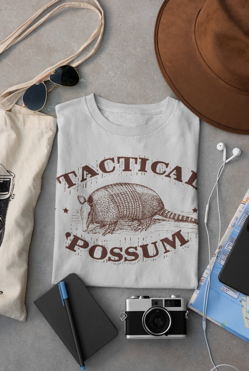 May include: A light gray t-shirt with a brown graphic of an armadillo and the text "Tactical Possum".