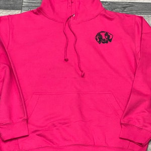 Op de afbeelding: Een roze hoodie met een geborduurd zwart dackel silhouet op de voorkant.