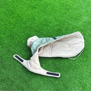 May include: A green and beige quilted dog coat with a fleece lining. The coat has a zipper closure and adjustable straps.